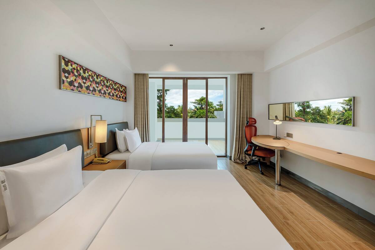 Habitación de hotel con dos camas, un escritorio, una silla, un ventanal grande y un cuadro en la pared.
