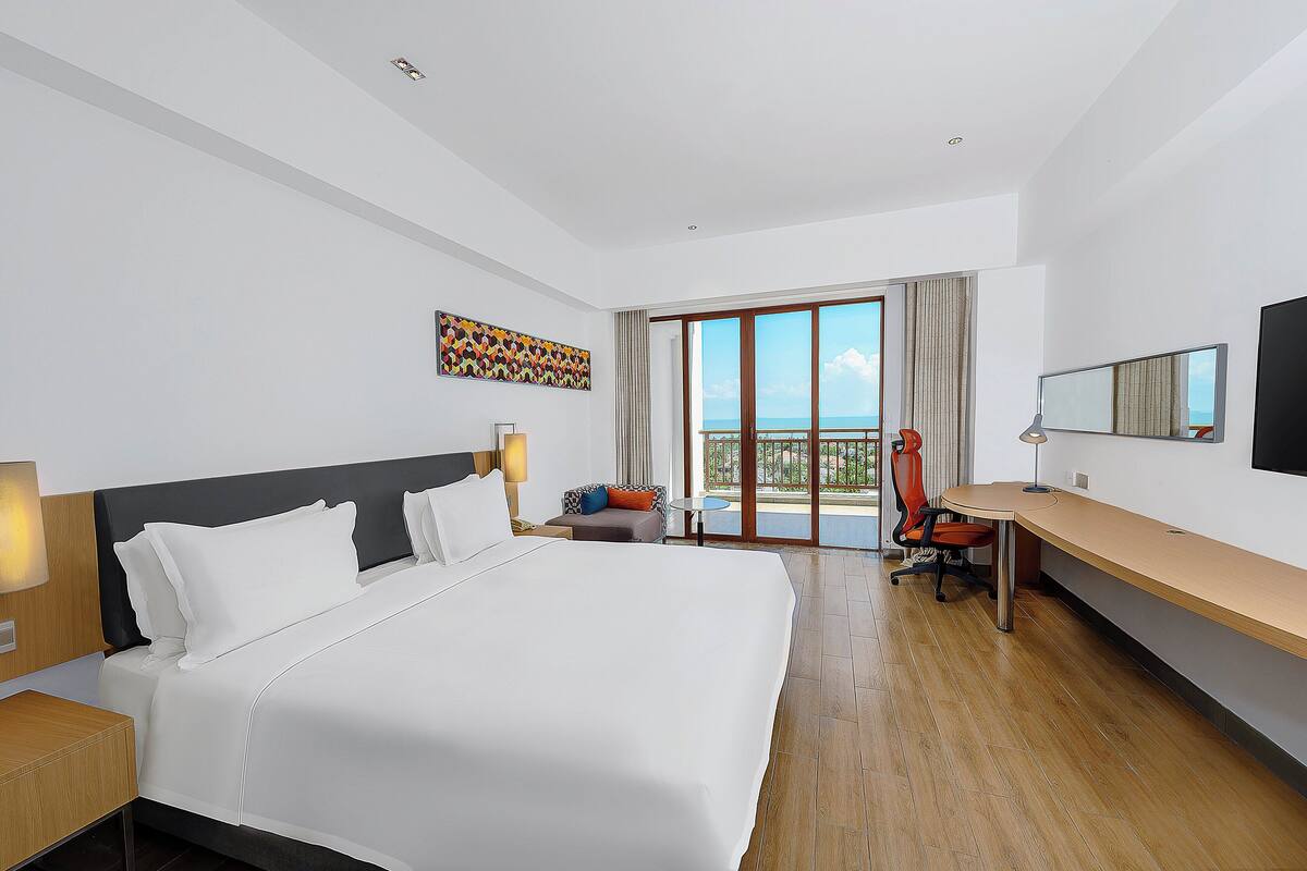 Una habitación de hotel moderna con una cama grande, un escritorio y un balcón con vistas.