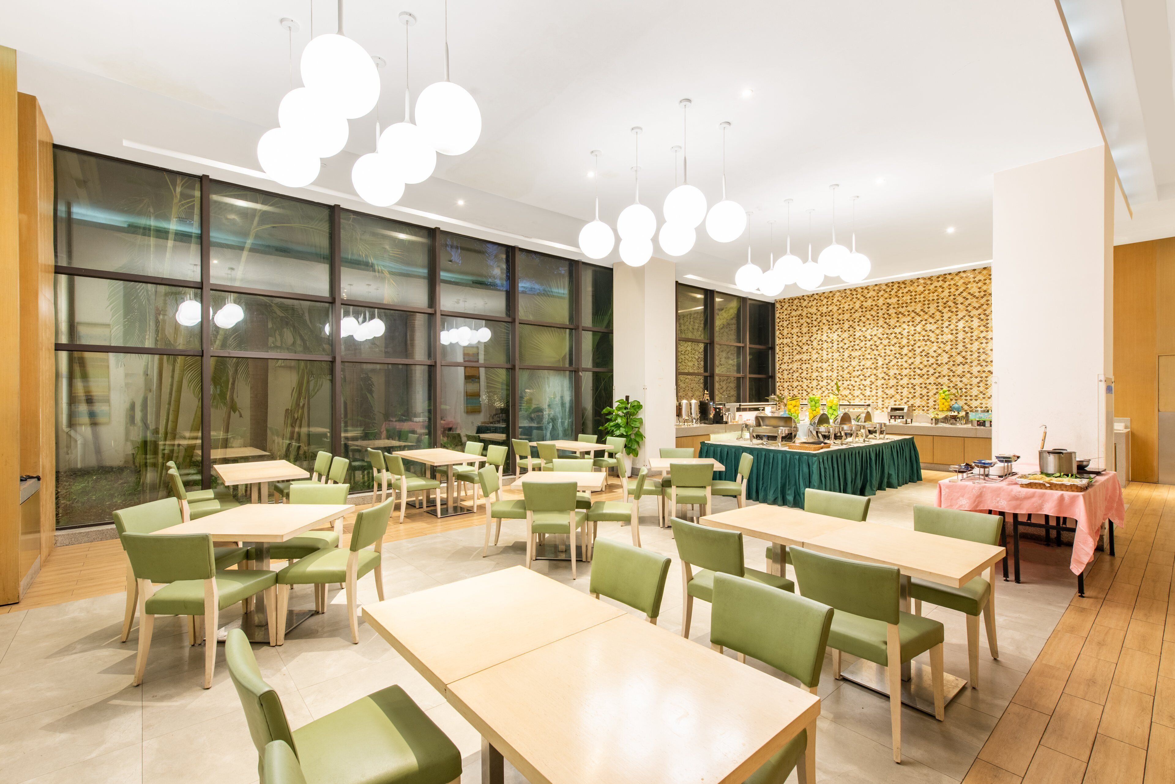 A modern dining area with multiple tables and chairs, large windows, and a kitchen area in the background.
