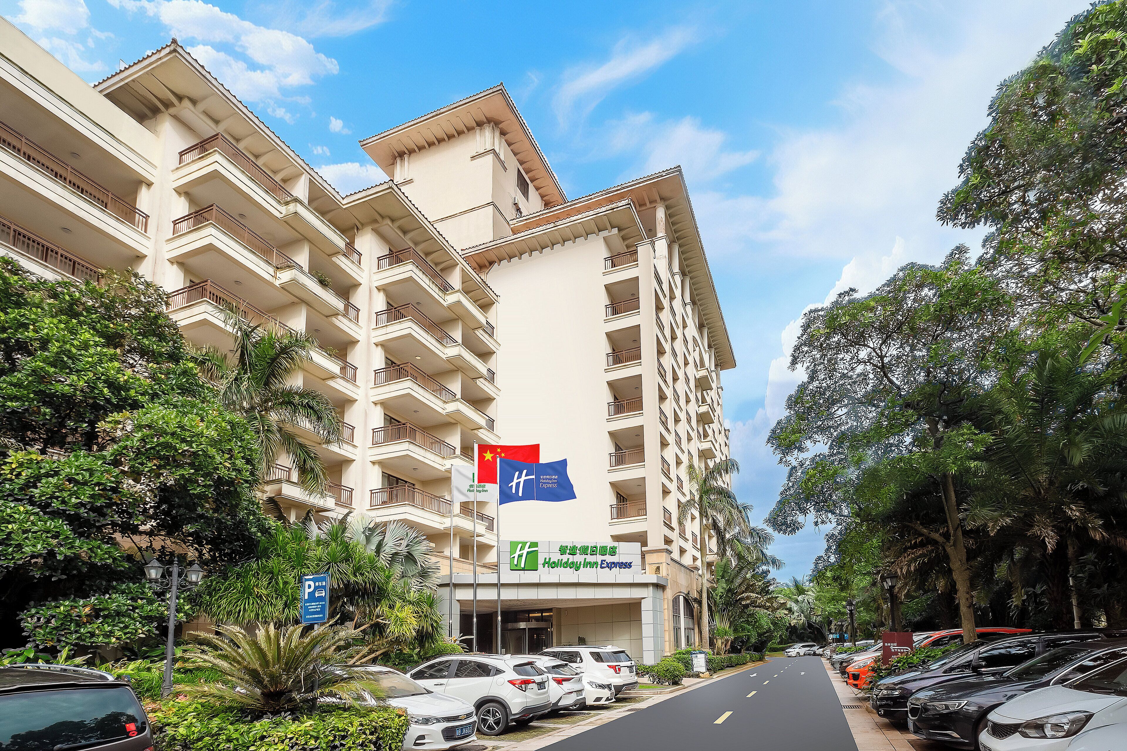 A multi-story hotel with a prominent Holiday Inn Express sign, surrounded by lush greenery and parked cars.