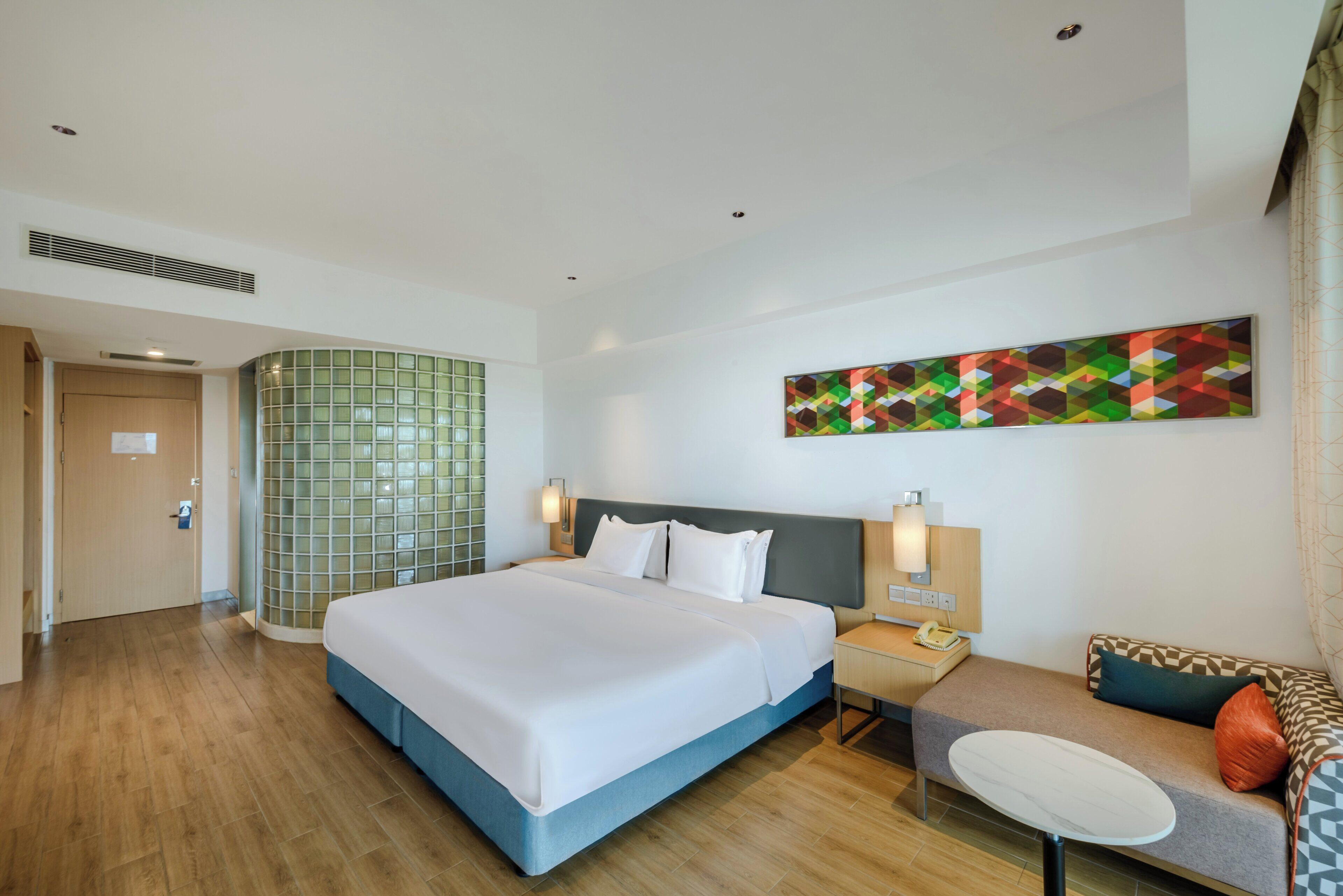 Quarto de hotel com uma cama grande, um sofá, uma mesinha e um telefone fixado na parede.
