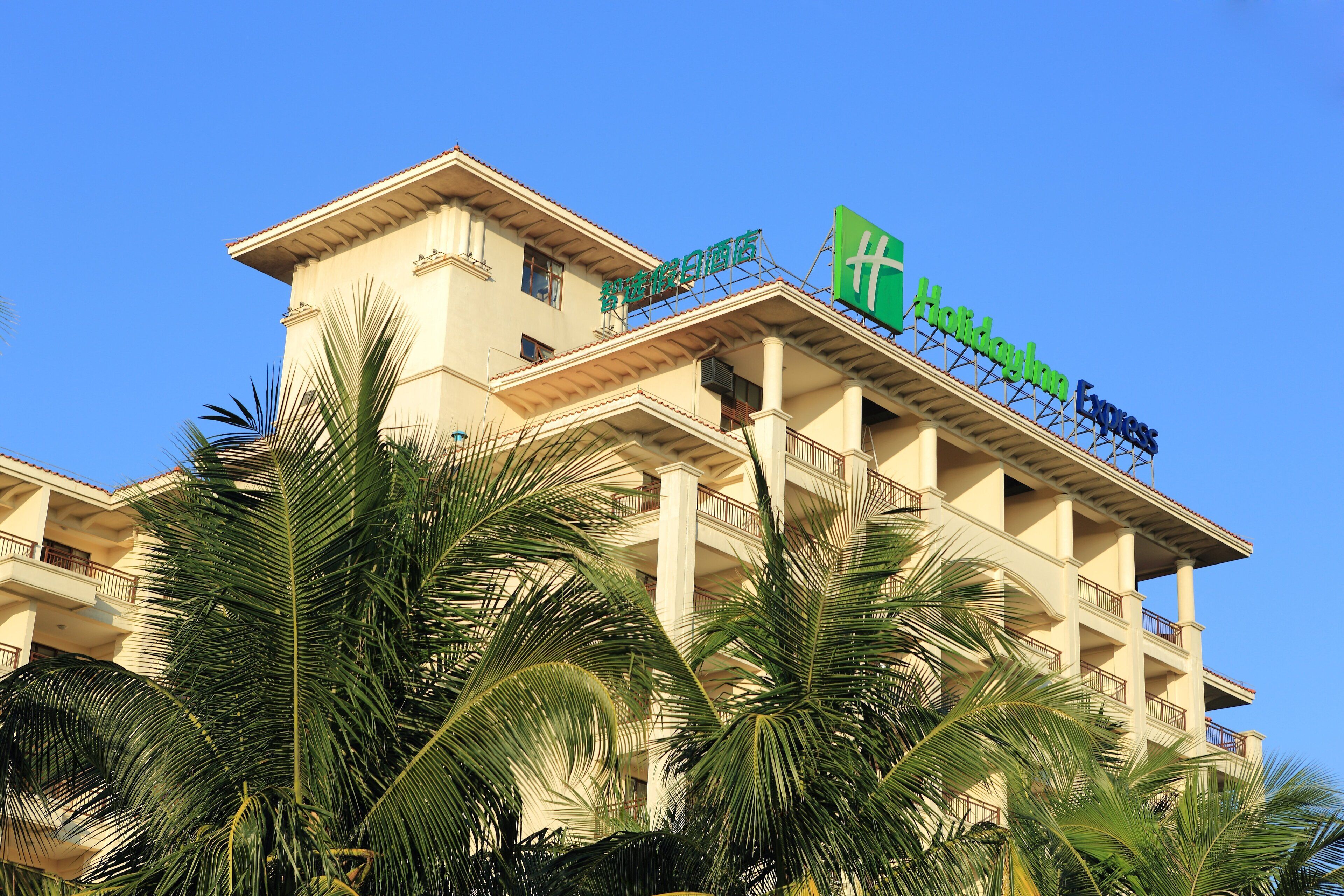 Un hotel con un llamativo letrero verde de Holiday Inn Express, que presenta un balcón y palmeras en primer plano.