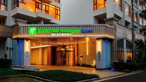 A hotel entrance with illuminated signage, a gated entrance, and a landscaped area with a pathway. - Holiday Inn Express Haikou West Coast by IHG (Haikou)