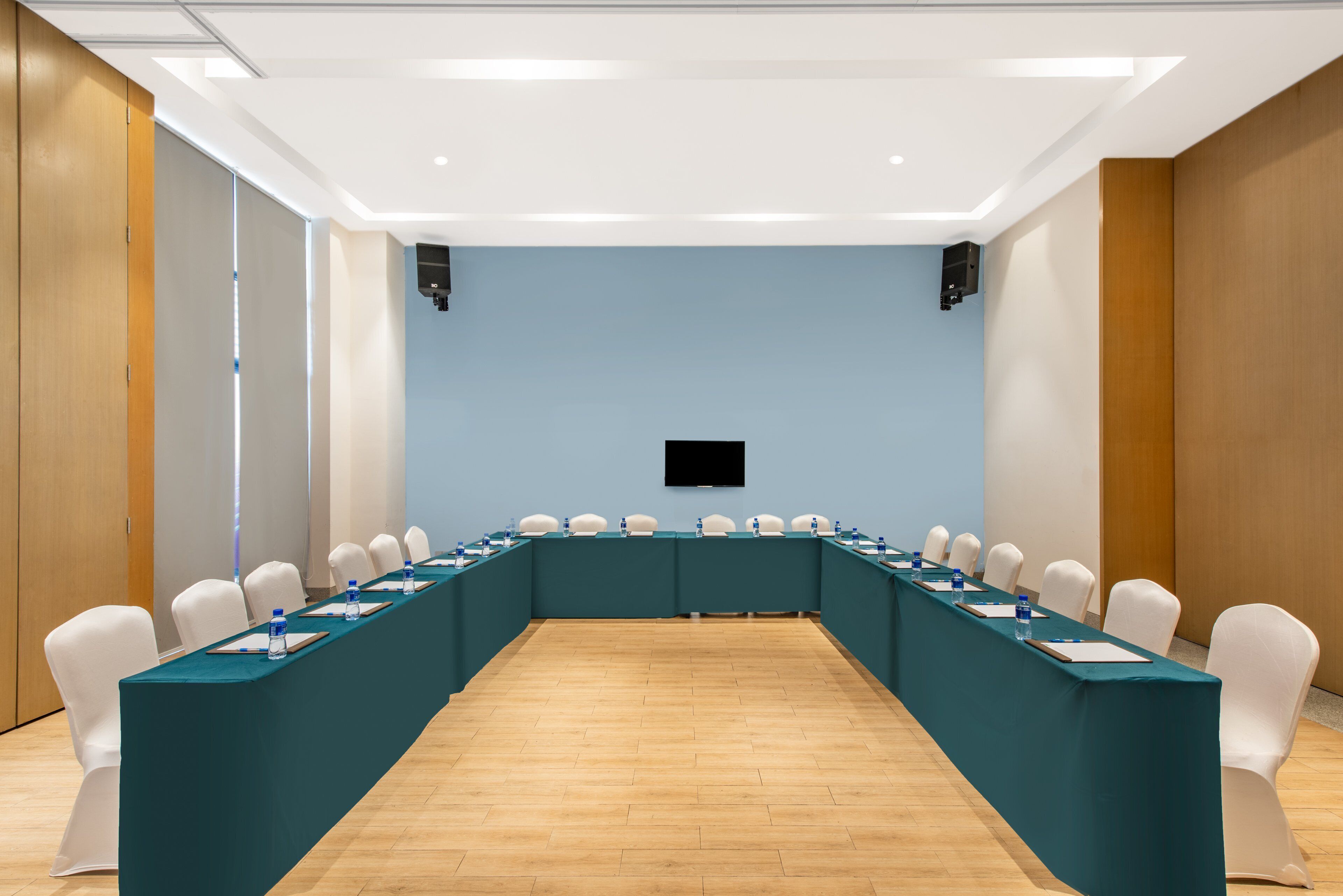 Una sala de conferencias con una larga mesa, sillas blancas y un televisor de pantalla plana en la pared.