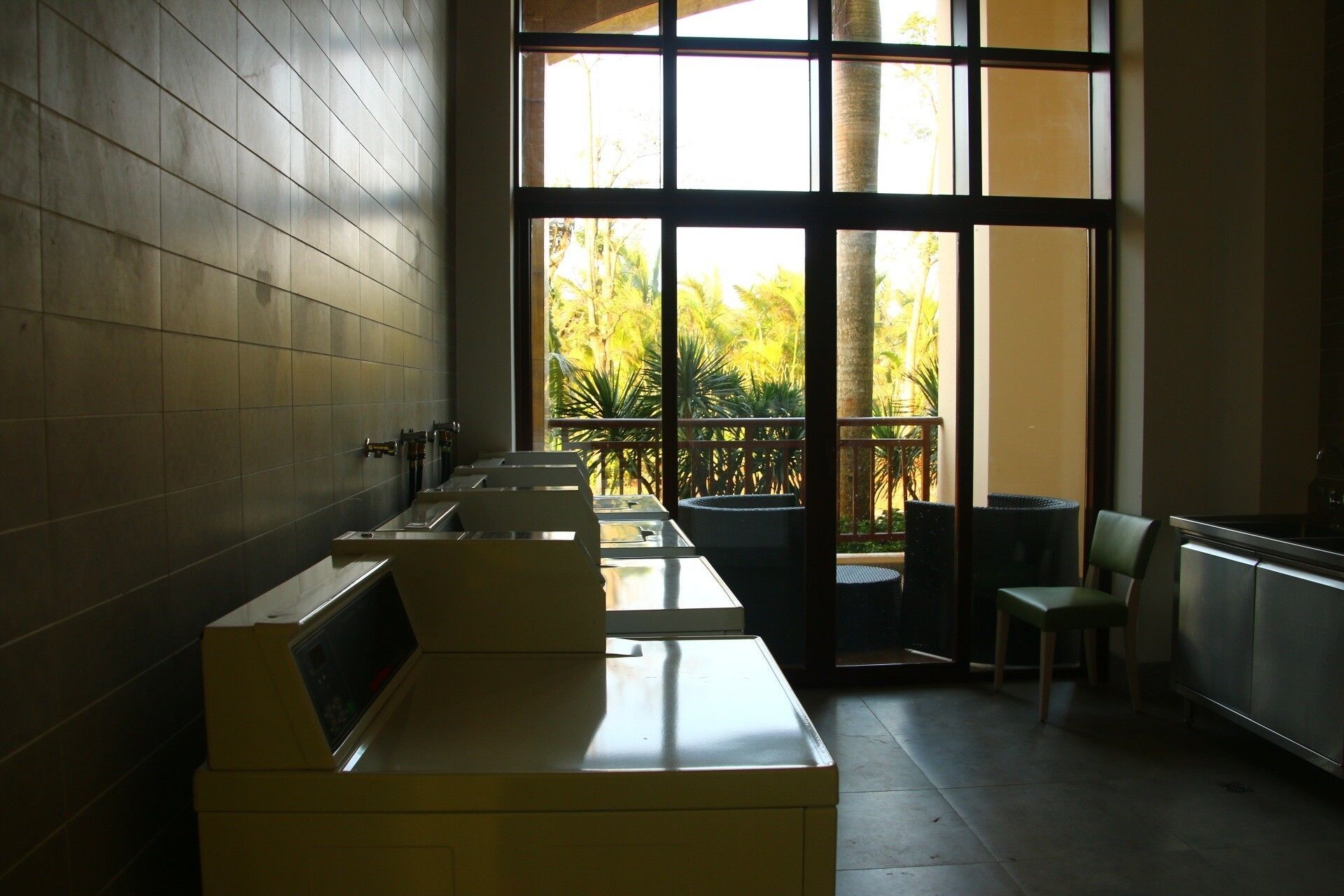 A public restroom with multiple sinks, a trash bin, and a seating area with chairs.