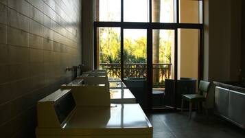 A public restroom with multiple sinks, a trash bin, and a seating area with chairs.