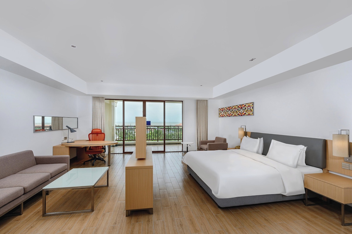 Een hotelkamer met een bed, een bureau, een bank en een balkon met uitzicht.