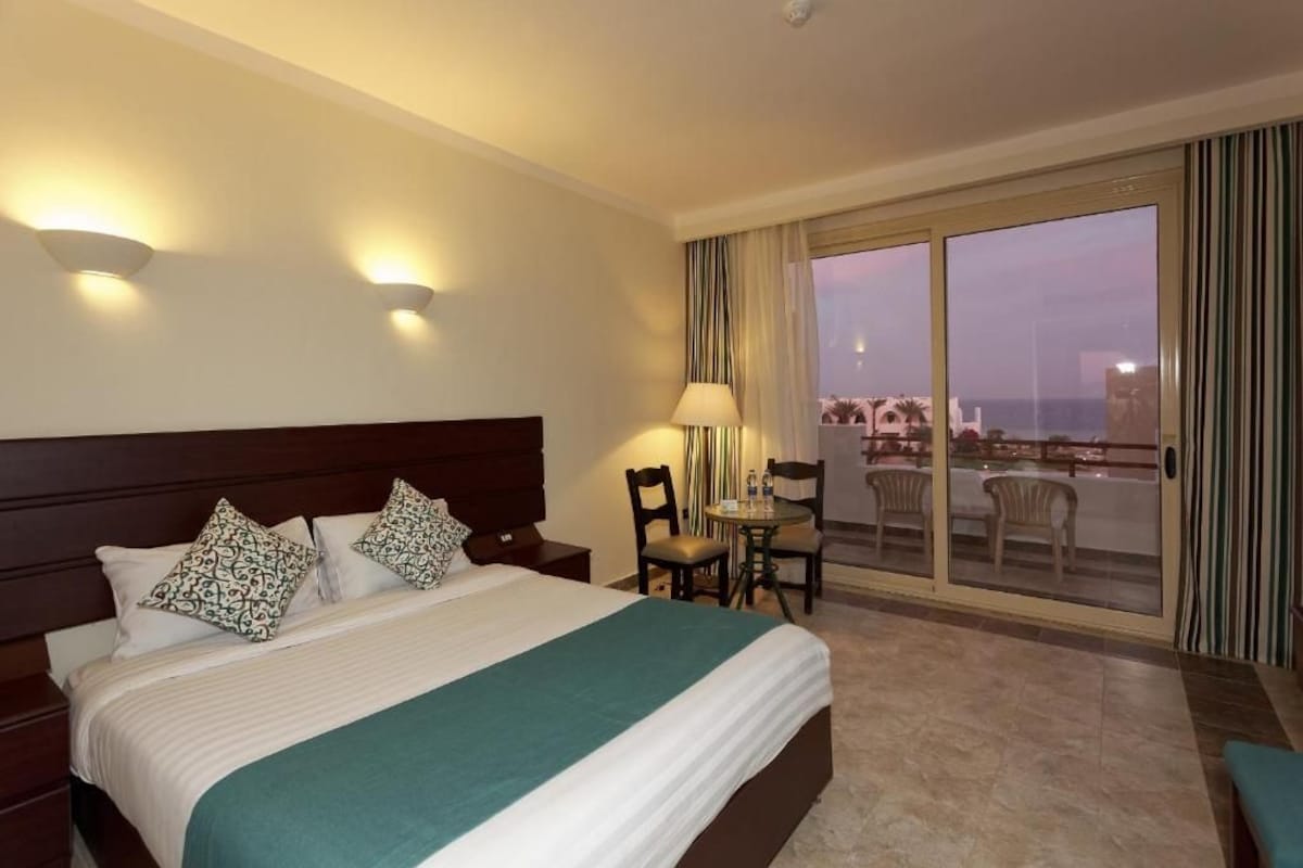 Habitación de hotel con cama, escritorio y vista a la ciudad a través de amplios ventanales correderas.