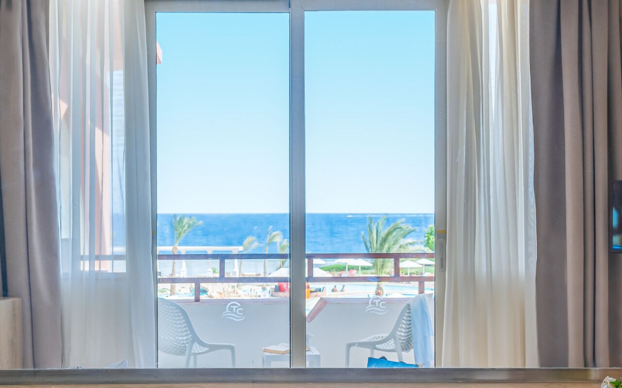 Ein Zimmer mit einer großen SchiebeglasTür, die auf einen Balkon mit Meer- und Strandblick führt.