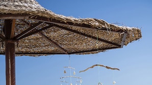 A beach scene with a thatched-roof structure, a table with food and drinks, and a person walking on the sand. - Three Corners Equinox Beach Resort (Marsa Alam)