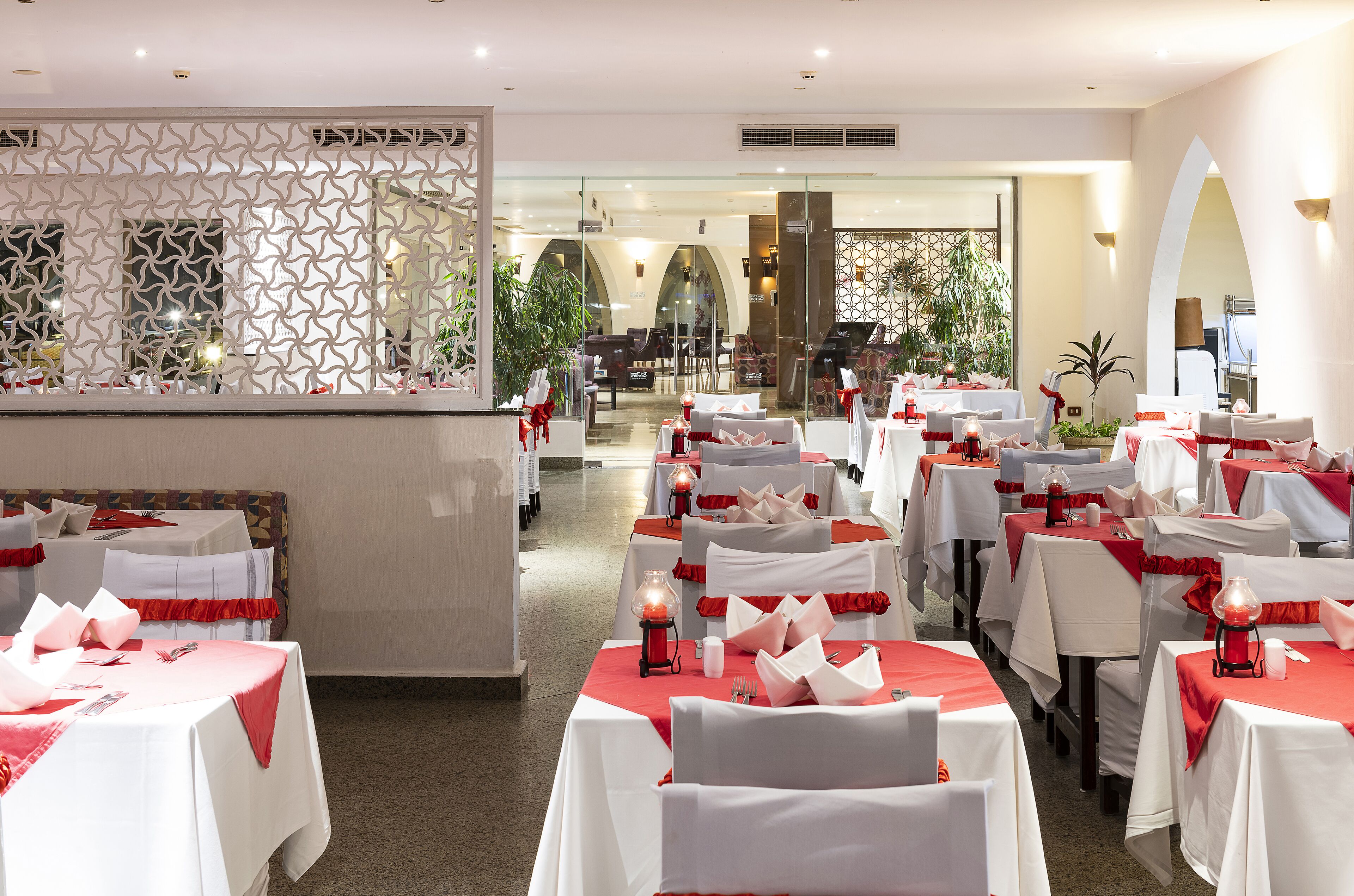 Un restaurante con mesas dispuestas para comer, con manteles blancos y detalles en rojo.