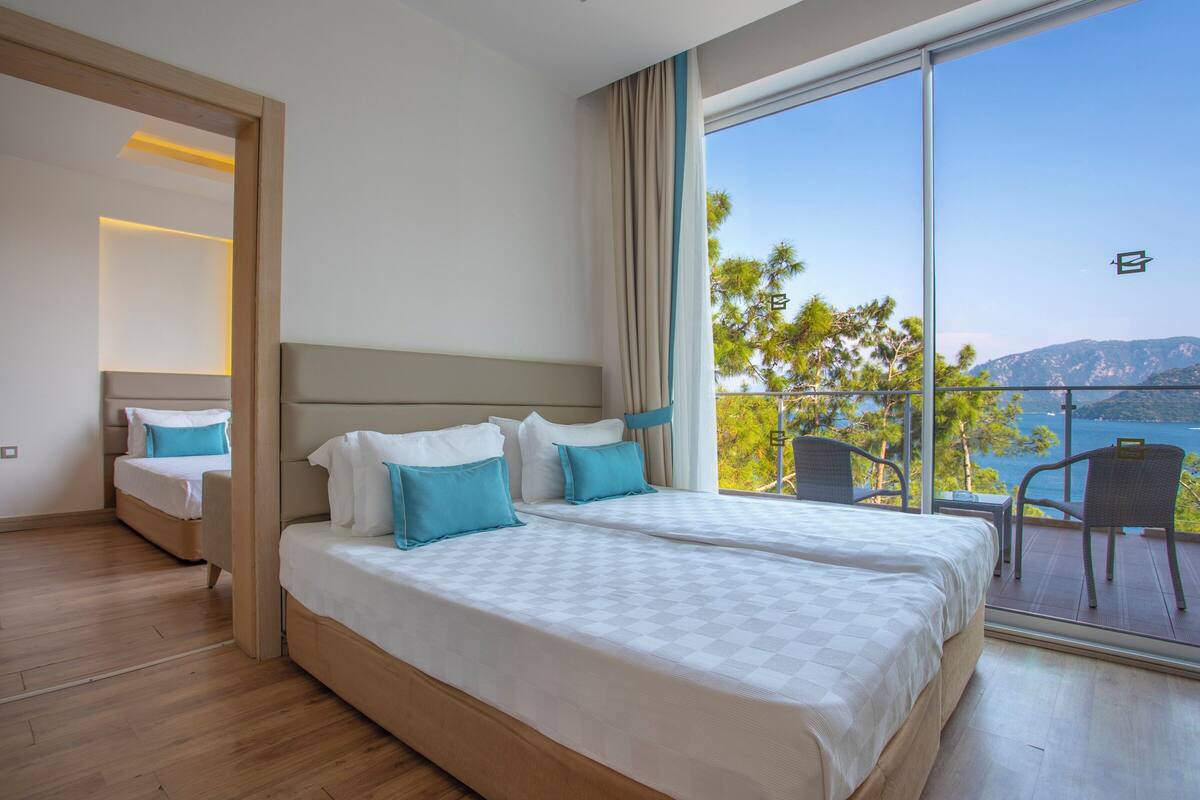 Une chambre d’hôtel avec deux lits, un balcon donnant sur la mer et un coin salon séparé.