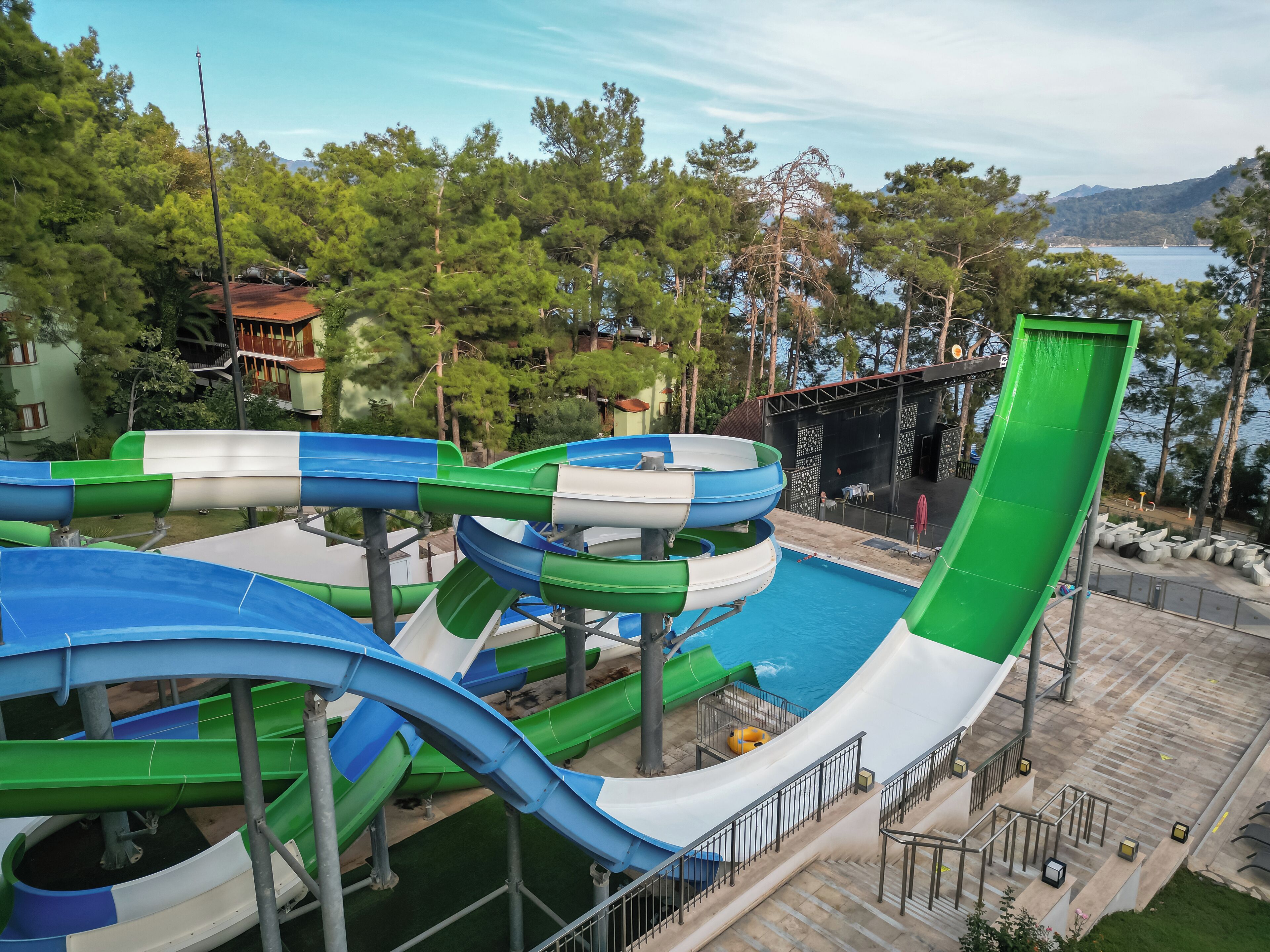 A water park with multiple slides and a pool area, surrounded by trees and a view of the sea.