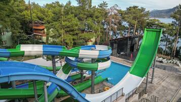 A water park with multiple slides and a pool area, surrounded by trees and a view of the sea.