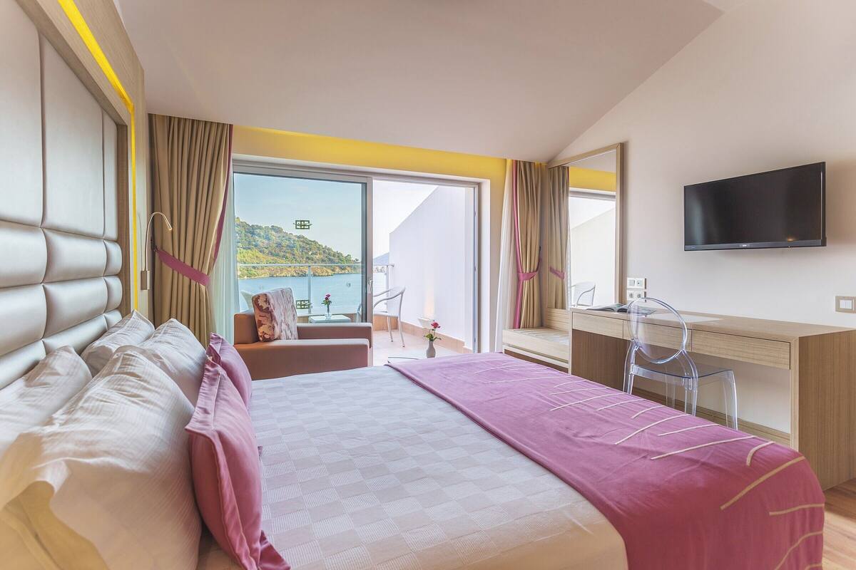 Une chambre d’hôtel avec un grand lit, un bureau, une chaise, une télévision et un balcon avec vue sur la mer.