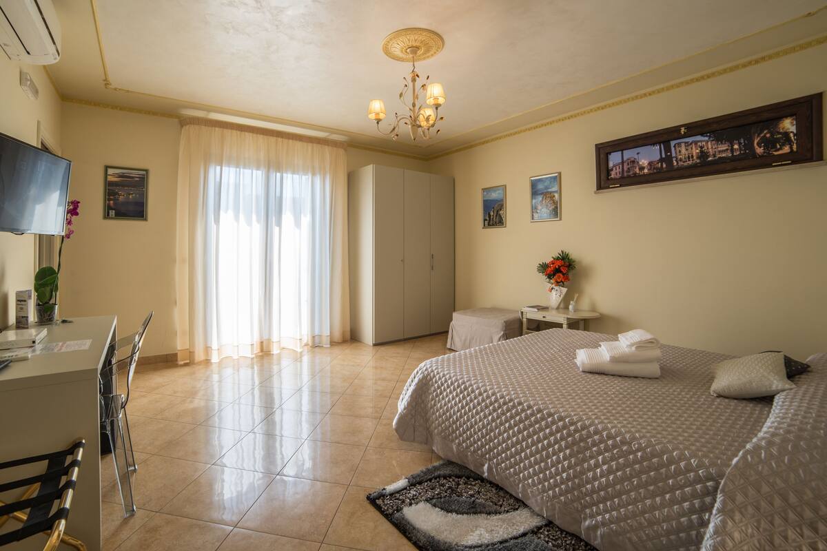 Habitació d'hotel amb un llit, escriptori, cadira, televisió, armari i finestra amb cortines.