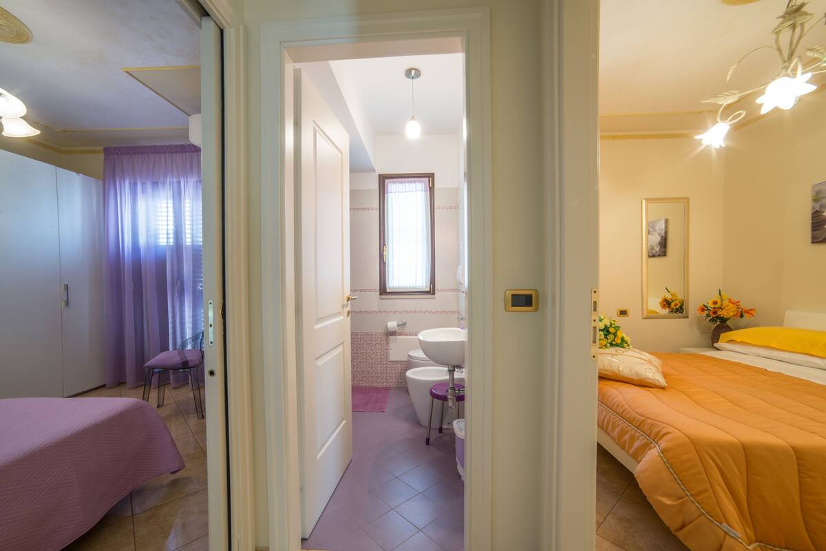 Habitació d'hotel amb un llit, un bany amb vàter i un lavabo, i una habitació separada amb escriptori i cadira.