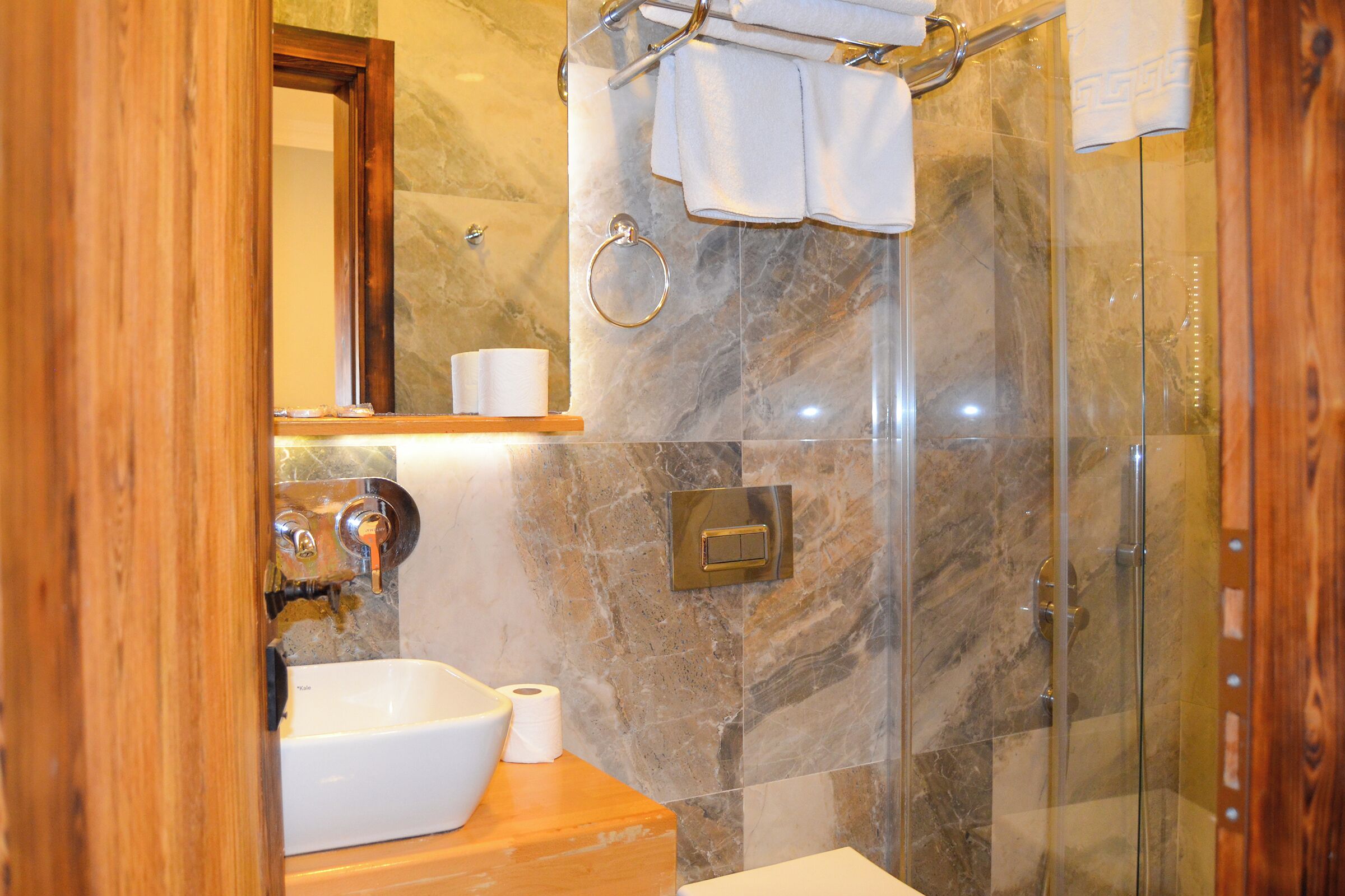 Une salle de bain avec un mur en marbre, un meuble-lavabo en bois, un lavabo, un miroir et une cabine de douche en verre.