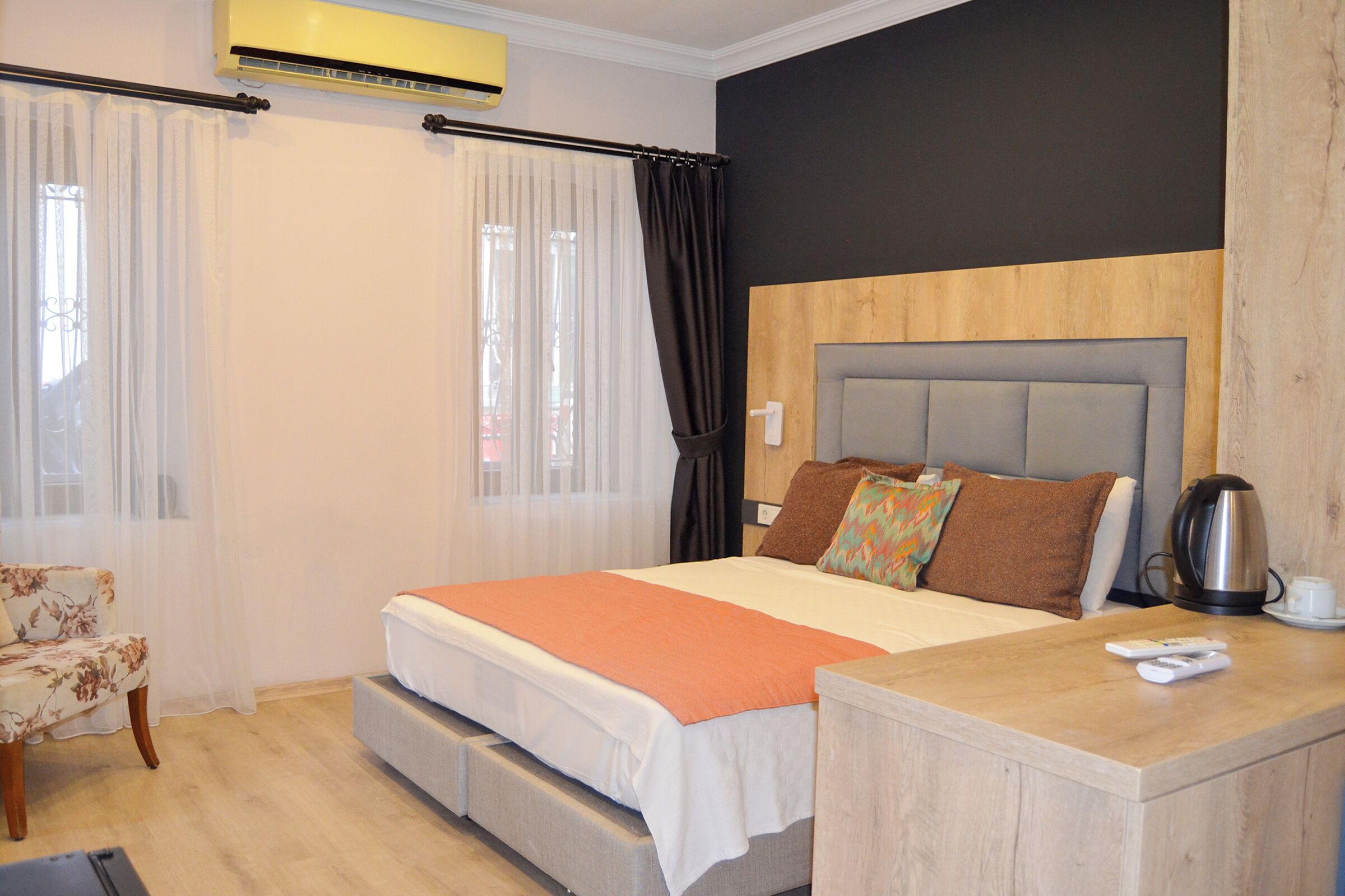 Une chambre moderne avec un lit, une chaise, une table de chevet avec une bouilloire et une fenêtre avec des rideaux.
