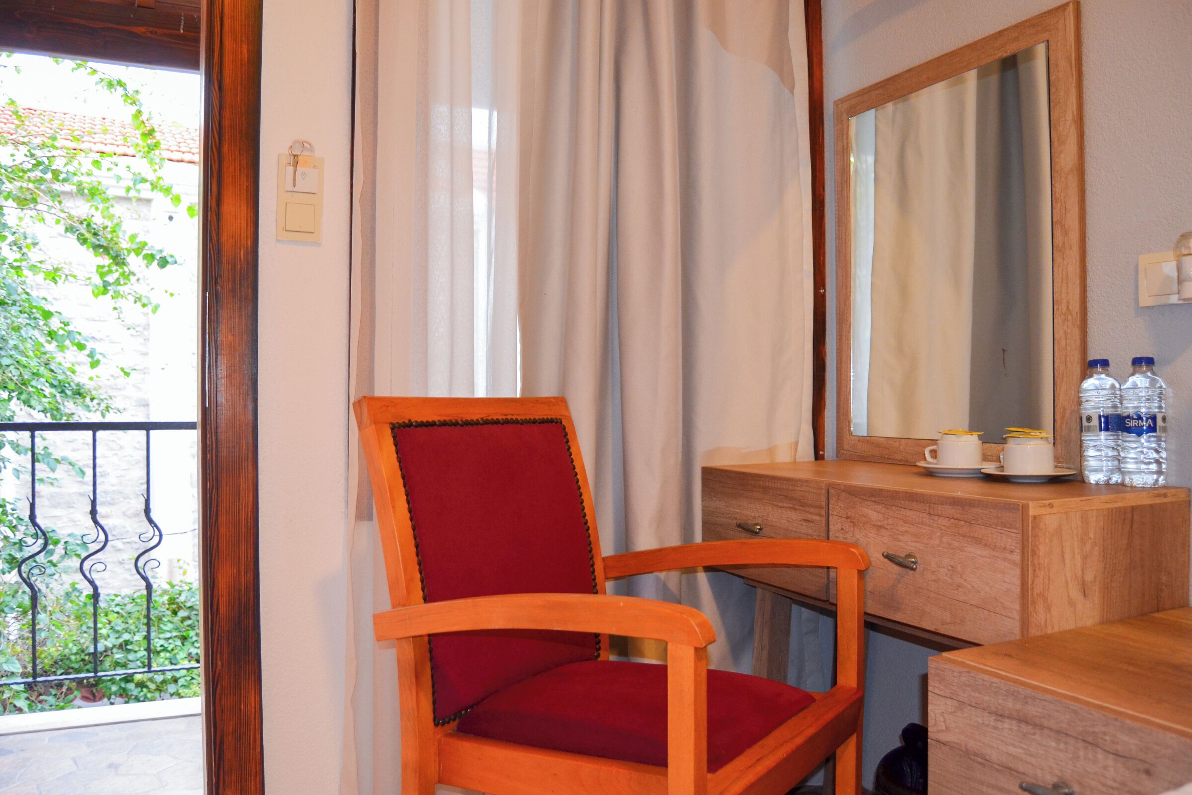 A wooden chair with a red cushion, a wooden dresser with a mirror, and two water bottles on top.