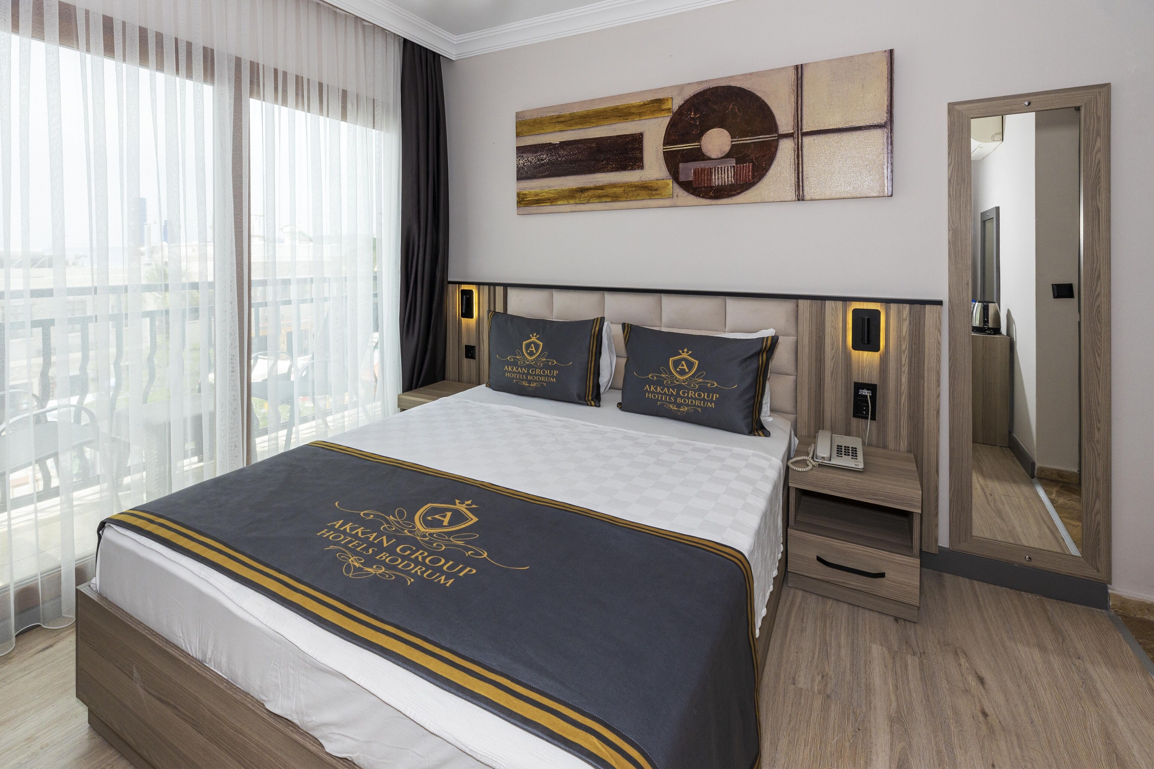 A hotel room with a large bed, a bedside table with a phone, and a mirror.