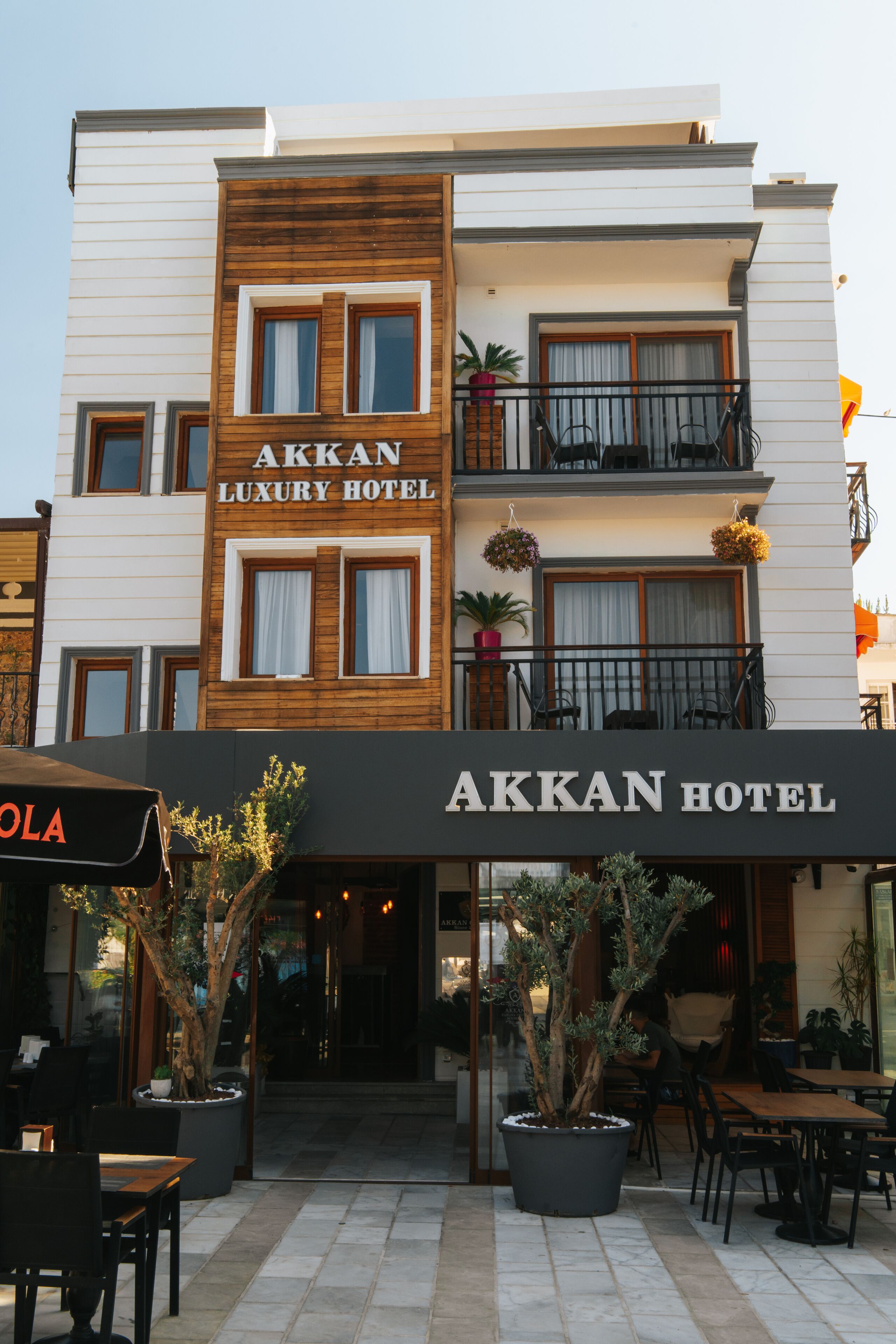 The exterior of the Aakkan Luxury Hotel with a modern design, featuring a large entrance, outdoor seating area, and potted plants.