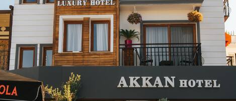 The exterior of the Aakkan Luxury Hotel with a modern design, featuring a large entrance, outdoor seating area, and potted plants.
