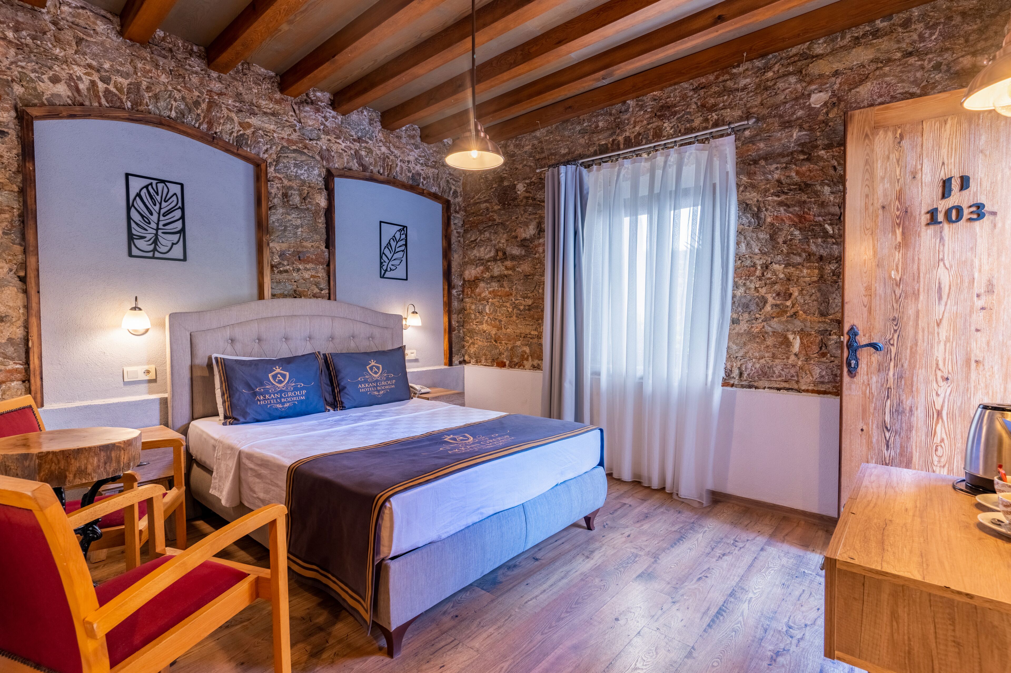 Un dormitorio con pared de piedra, una cama con cabecera, una mesa de madera y una silla.