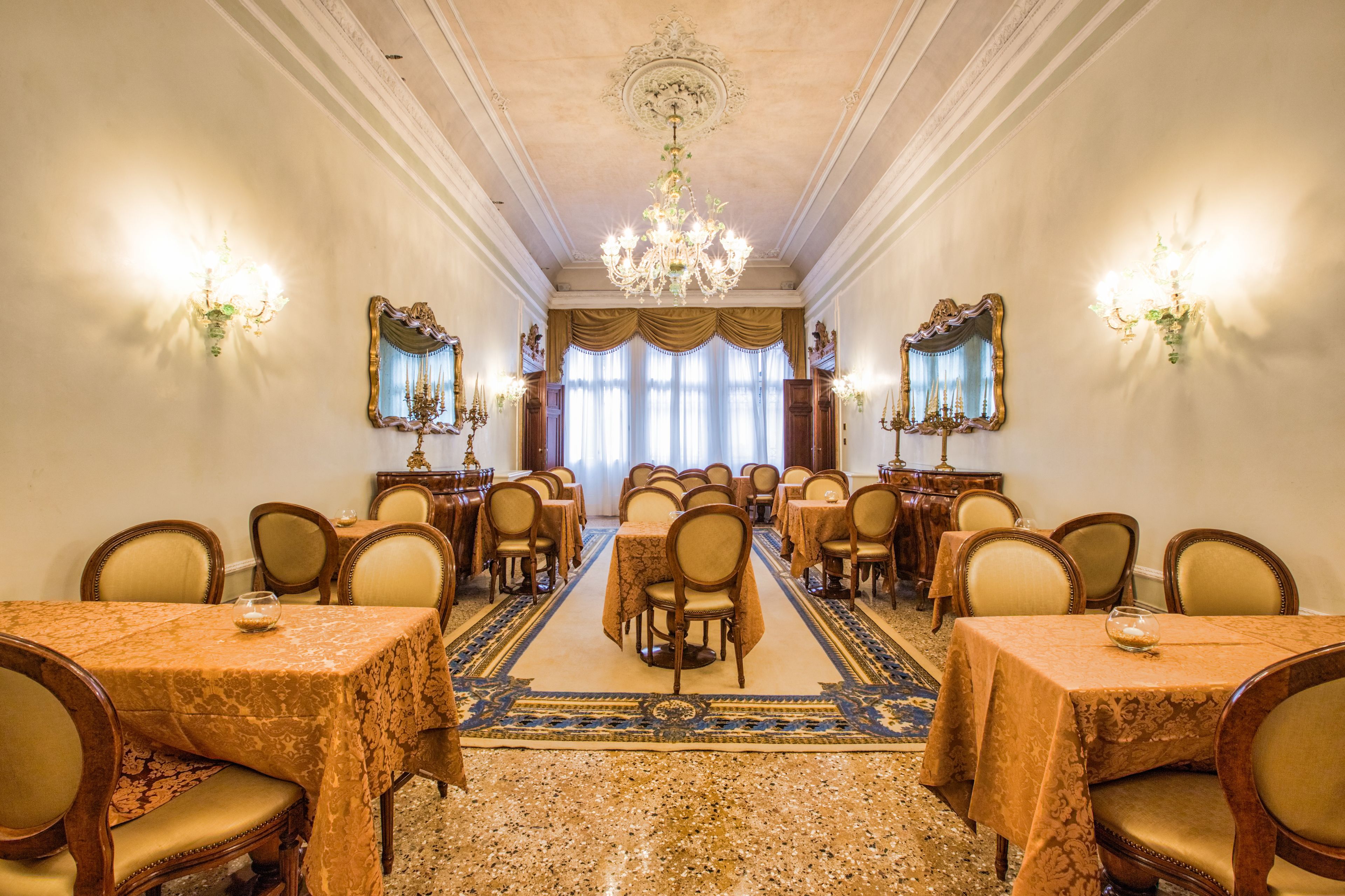 Une salle à manger élégante, dotée de plusieurs tables et chaises, de lustres somptueux et d’appliques murales décoratives.