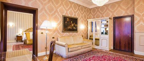 A room with a patterned wallpaper, a chandelier, a sofa, a cabinet, and a large rug.