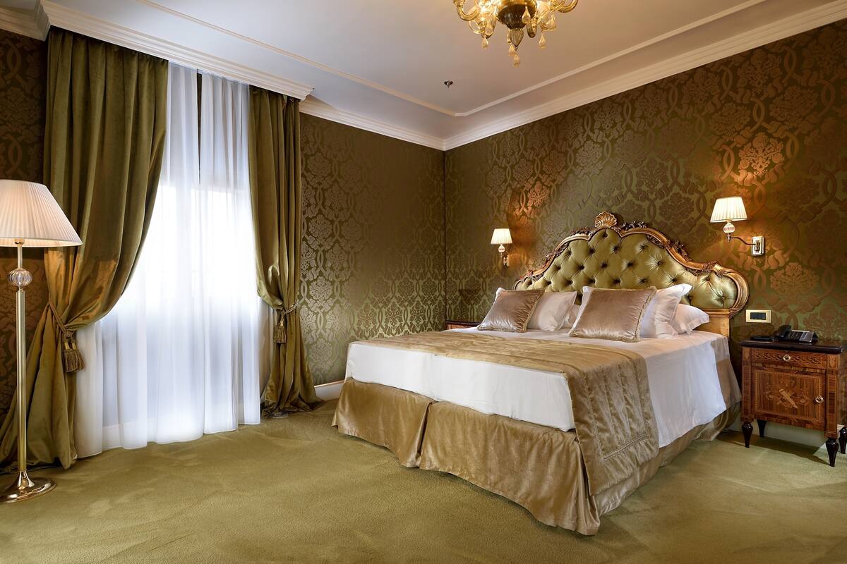 Una cama grande con cabecera capitonada, dos lámparas de noche y una mesita de noche con teléfono.