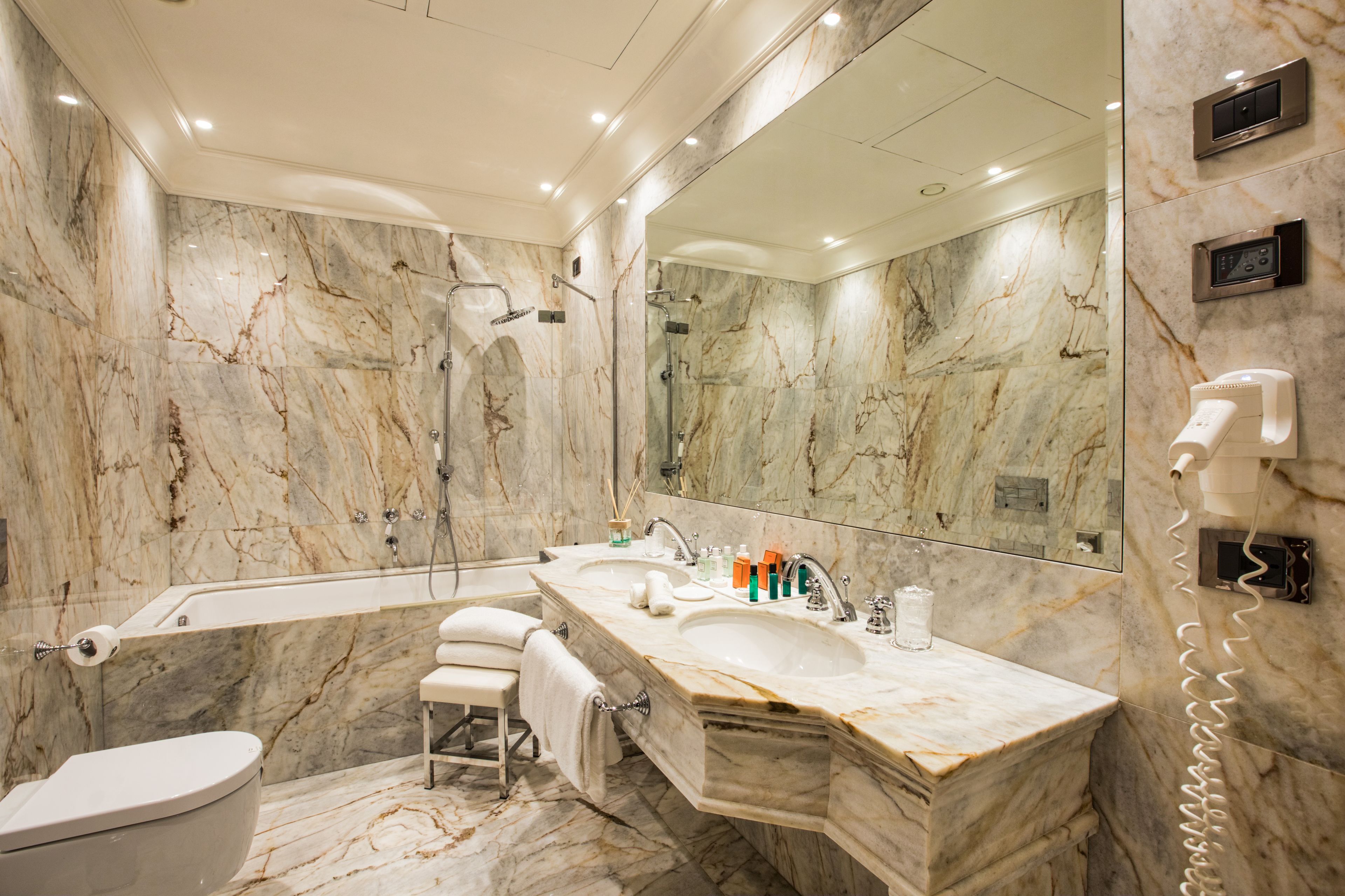 A modern bathroom with a marble vanity, a bathtub, a toilet, and a large mirror.