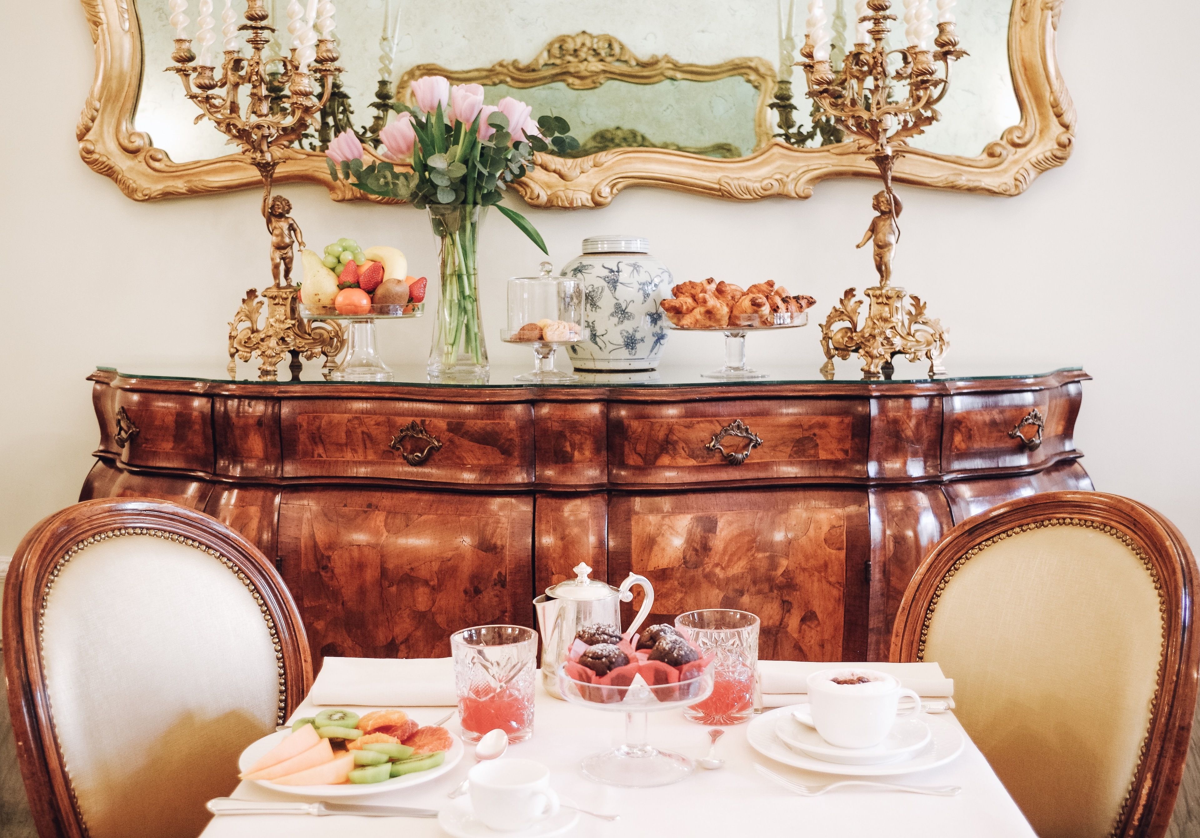 Une table à manger dressée avec divers plats, un vase rempli de fleurs et un miroir décoratif au-dessus.