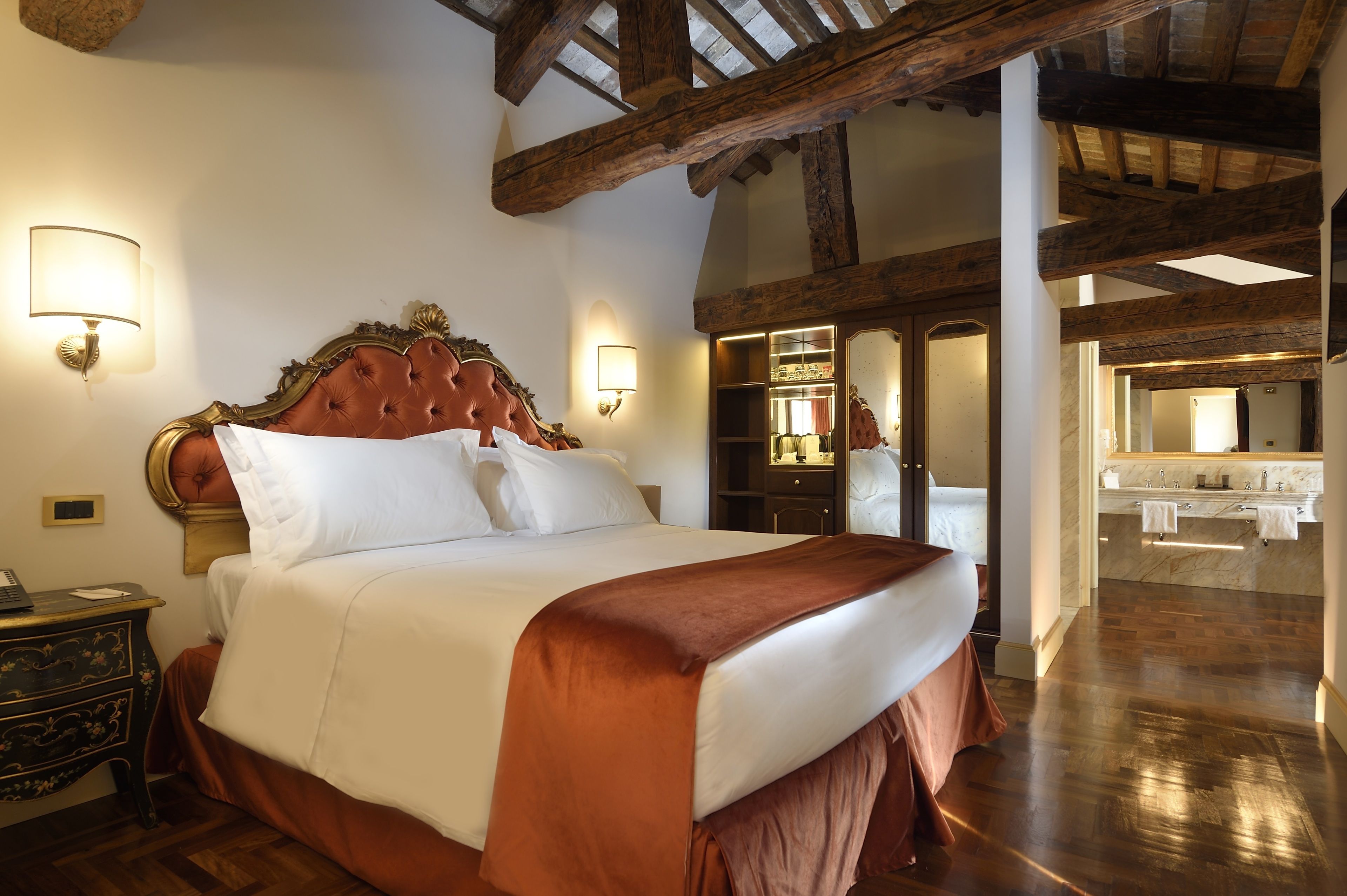Una cama grande con cabecera de madera, dos lámparas de noche y una mesita de noche con un teléfono.