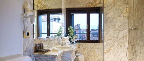 A bathroom with a marble sink, a glass shower enclosure, and a view of buildings through large windows.
