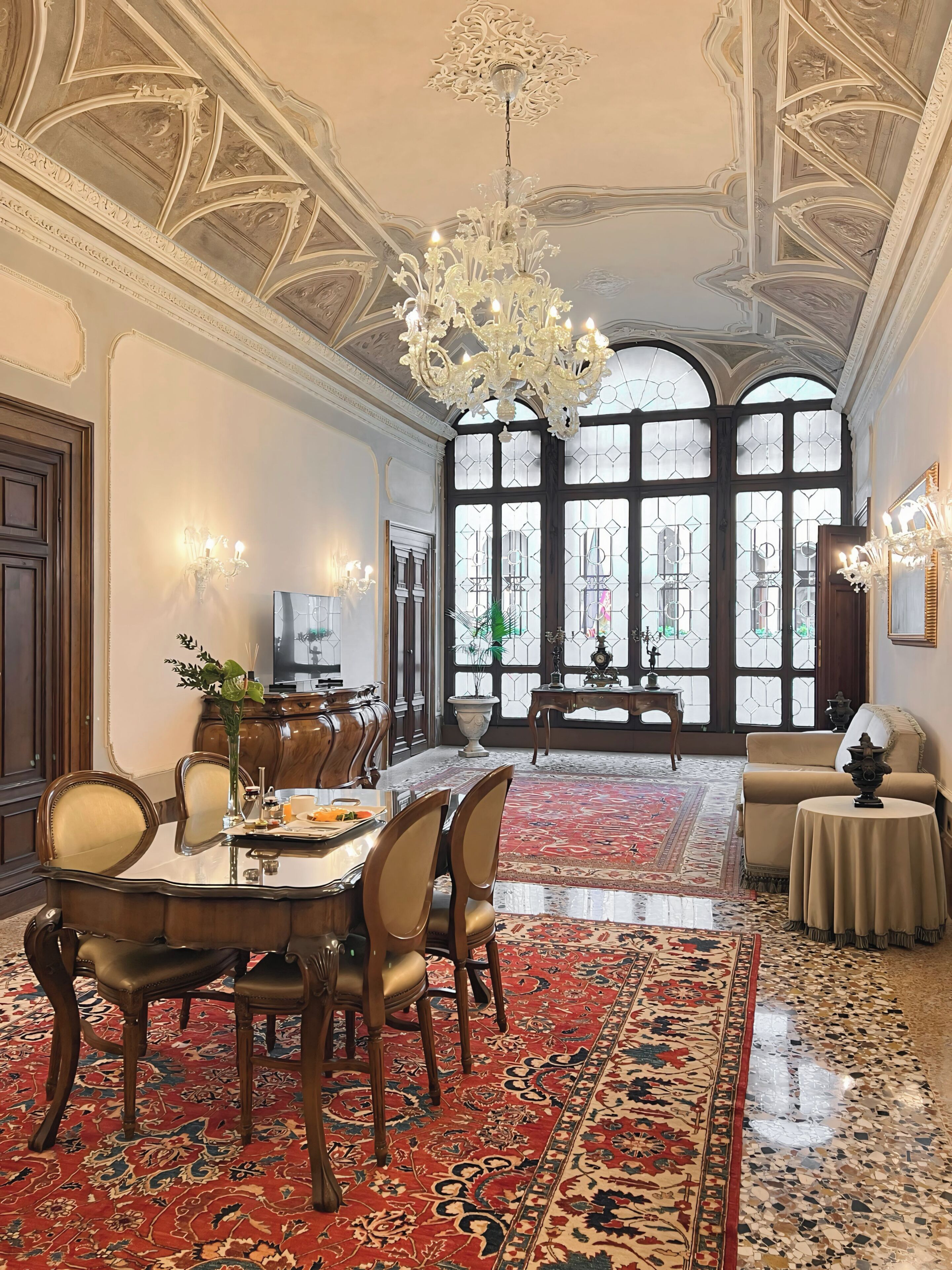 Un comedor amplio y elegante con candelabro, techo decorado y ventanas grandes.