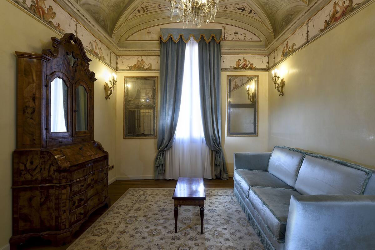 Una habitación con un aparador de madera, un sofá, una mesita y un ventanal con cortinas.