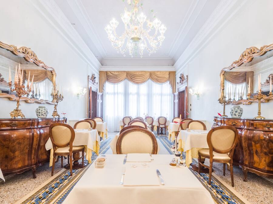 Una sala da pranzo formale con lampadari decorati, grandi specchi e un lungo tavolo apparecchiato per un pasto.