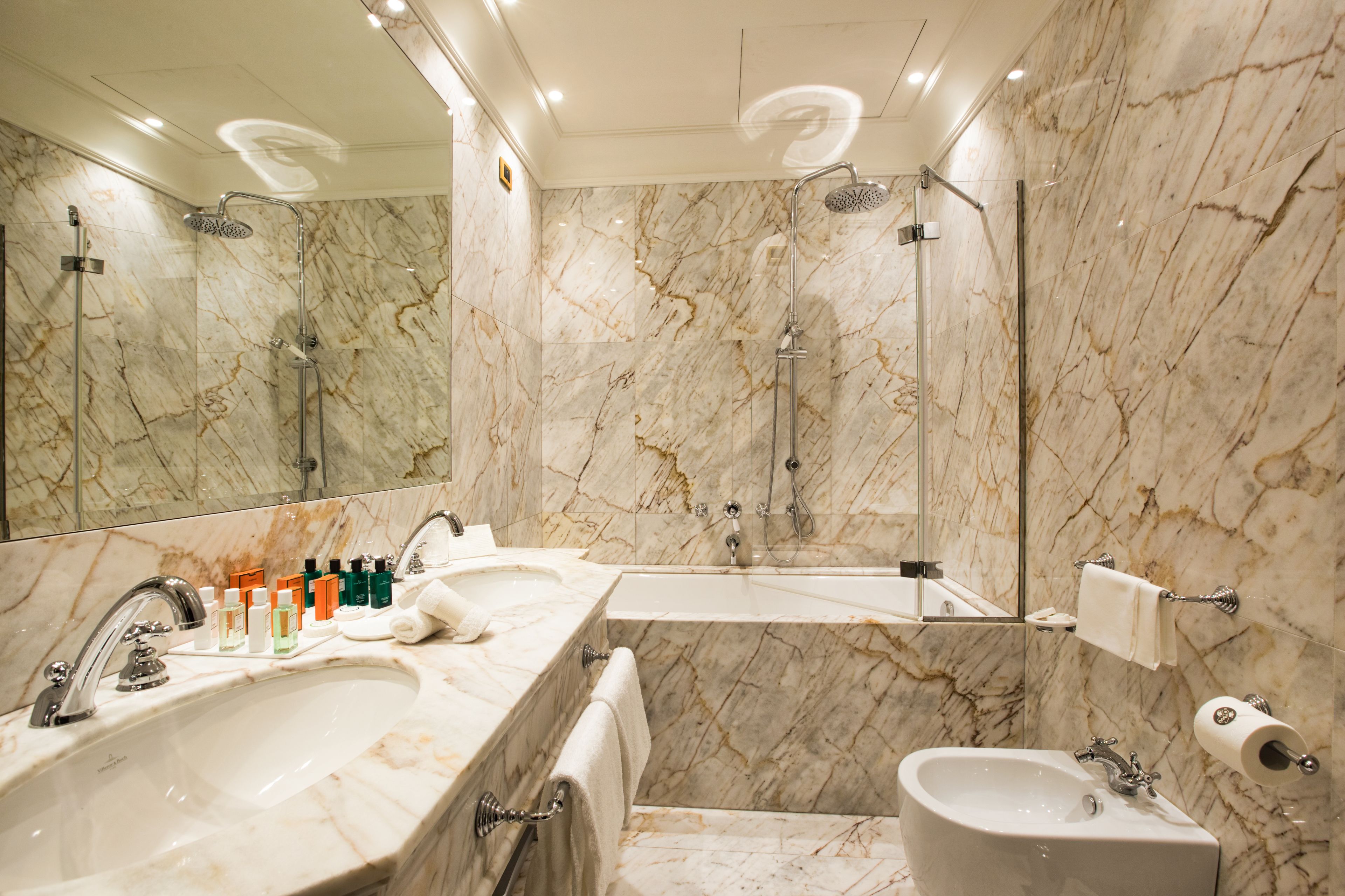 A bathroom with a large marble sink, a separate basin, a shower with a handheld showerhead, and a mirror.
