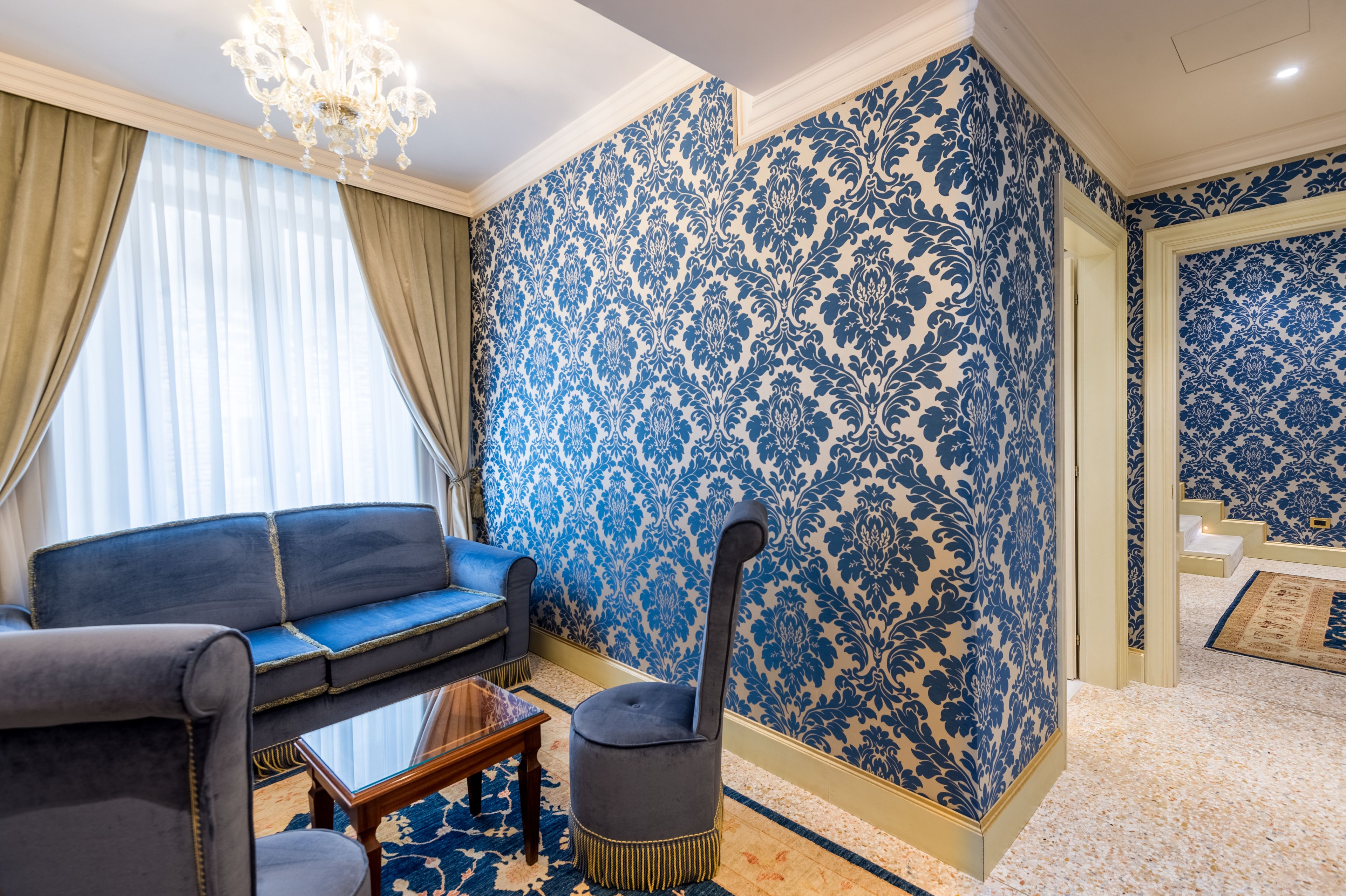A room with a blue patterned wallpaper, a blue sofa, a small table, and a chair.
