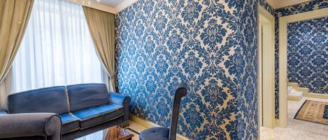 A room with a blue patterned wallpaper, a blue sofa, a small table, and a chair.