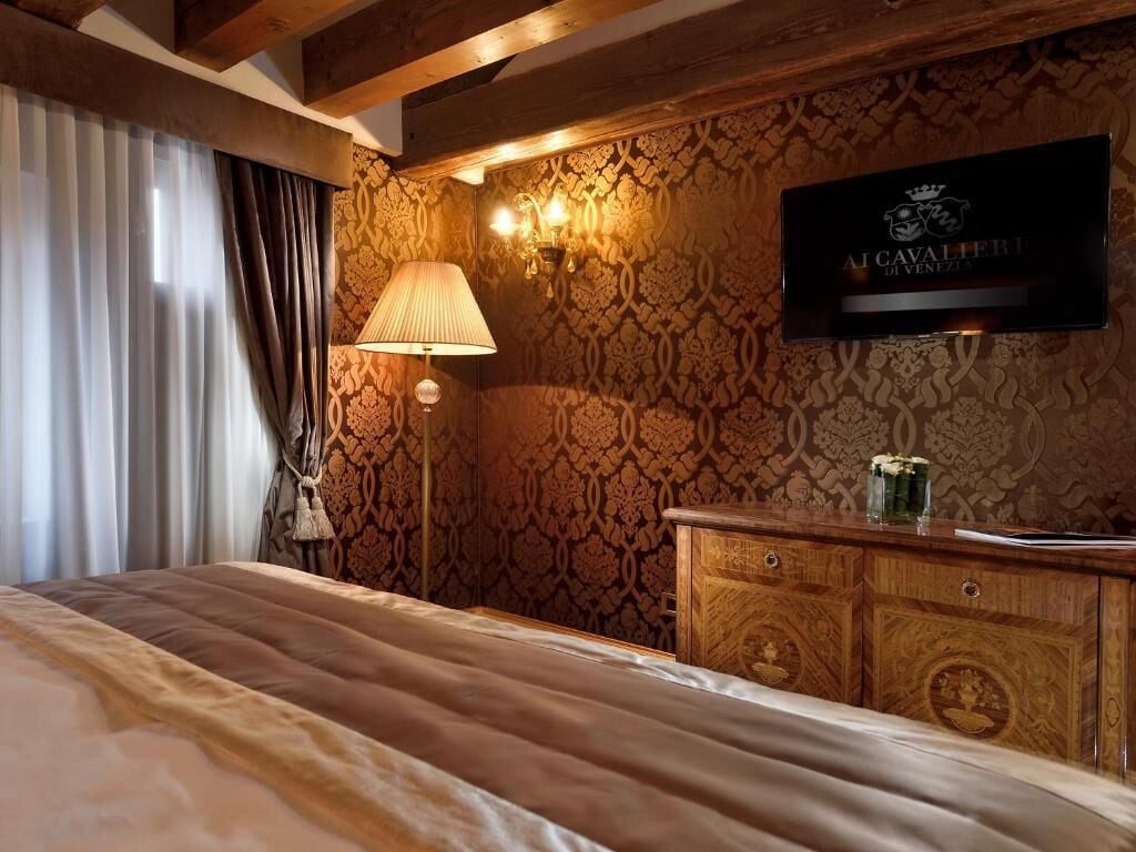 Una habitación de hotel con una cama, un tocador de madera, una lámpara y un televisor fijado a la pared.