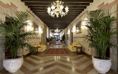 A grand hallway with a high ceiling, chandeliers, and potted plants.