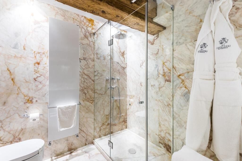 A modern bathroom with a glass-enclosed shower, marble walls, and a white bathtub.
