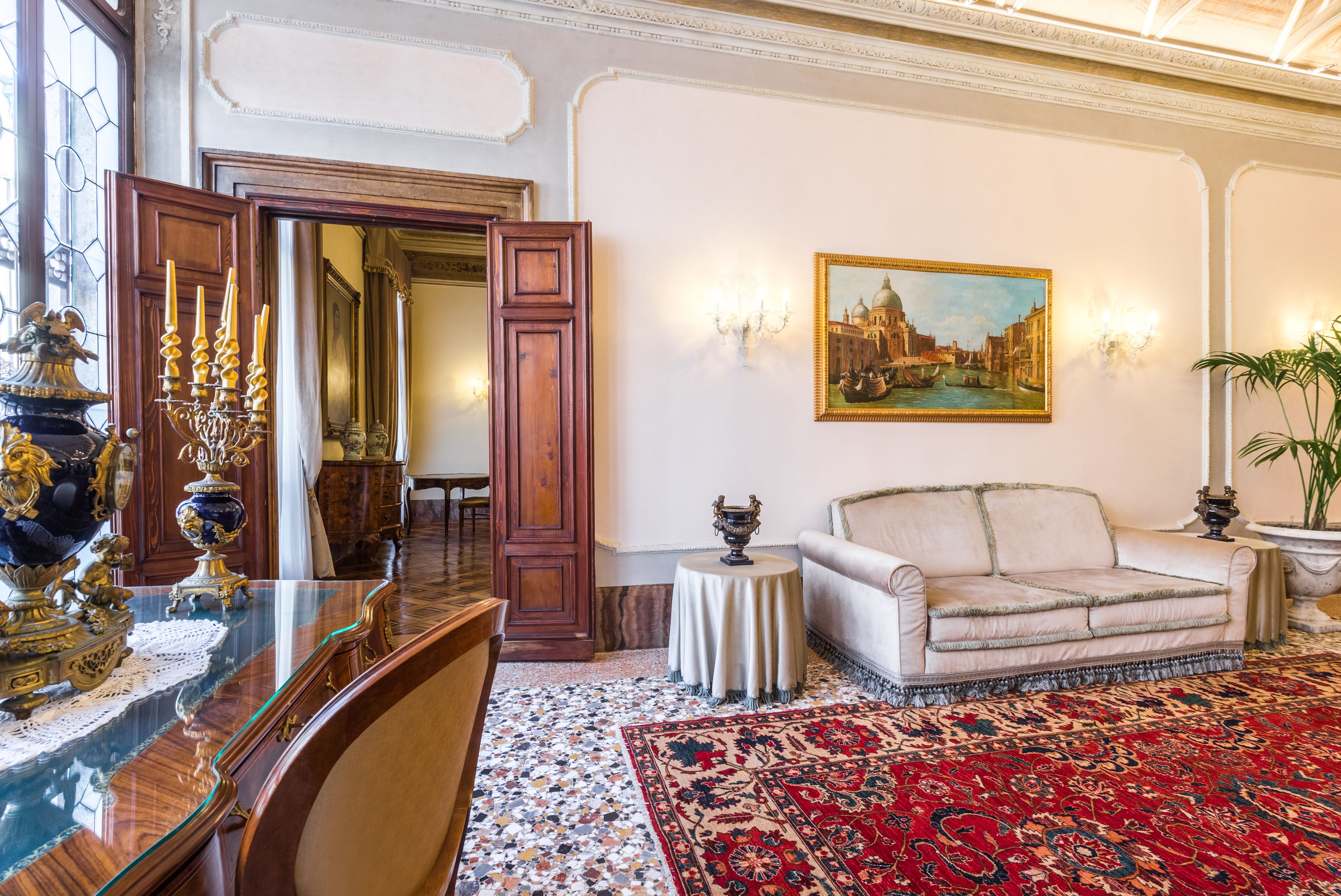 A room with a wooden table, a cream-colored sofa, a patterned rug, and a painting of a cityscape.