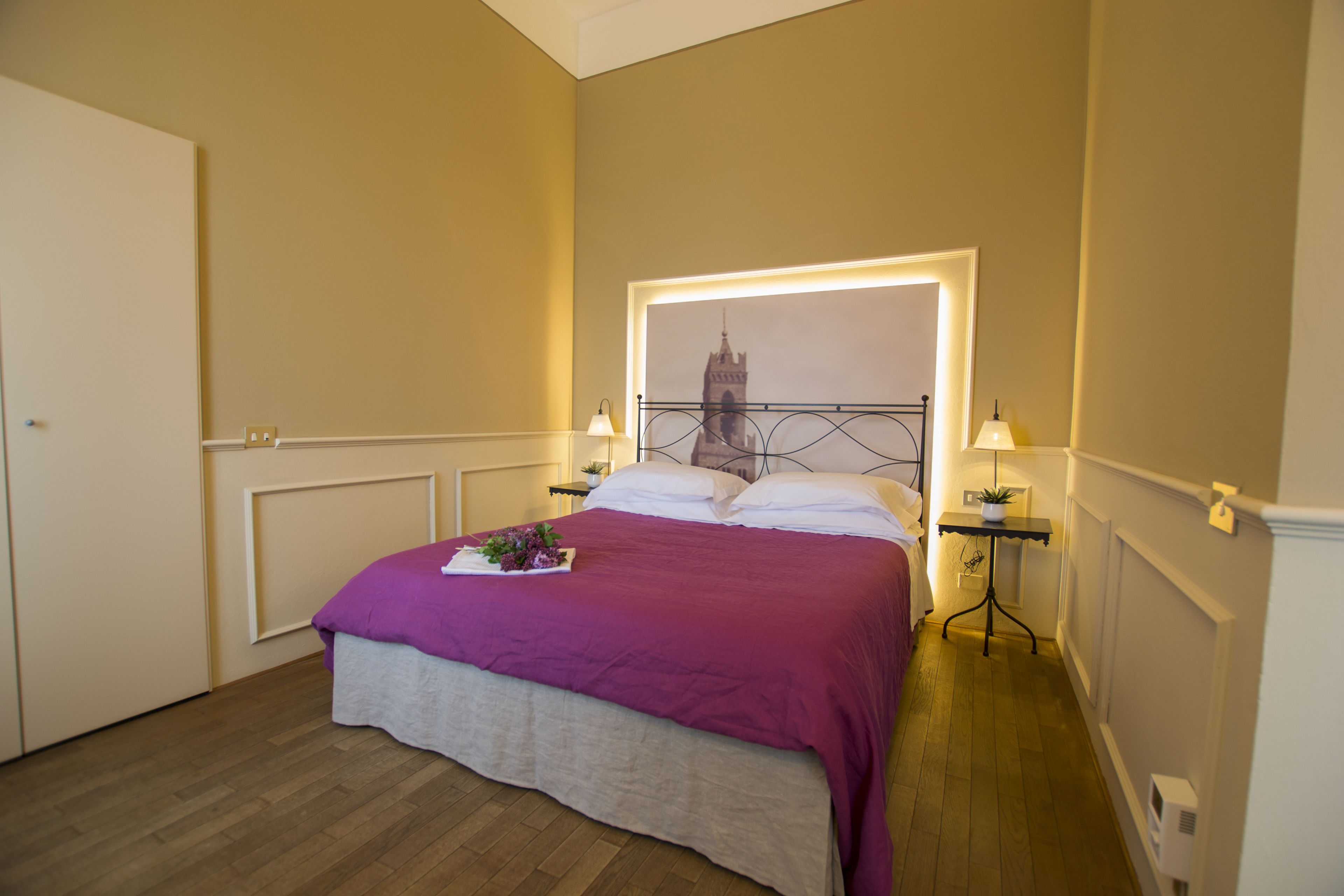 Quarto bem arrumado com uma cama, uma mesa de cabeceira com abajur e um quadro na parede.