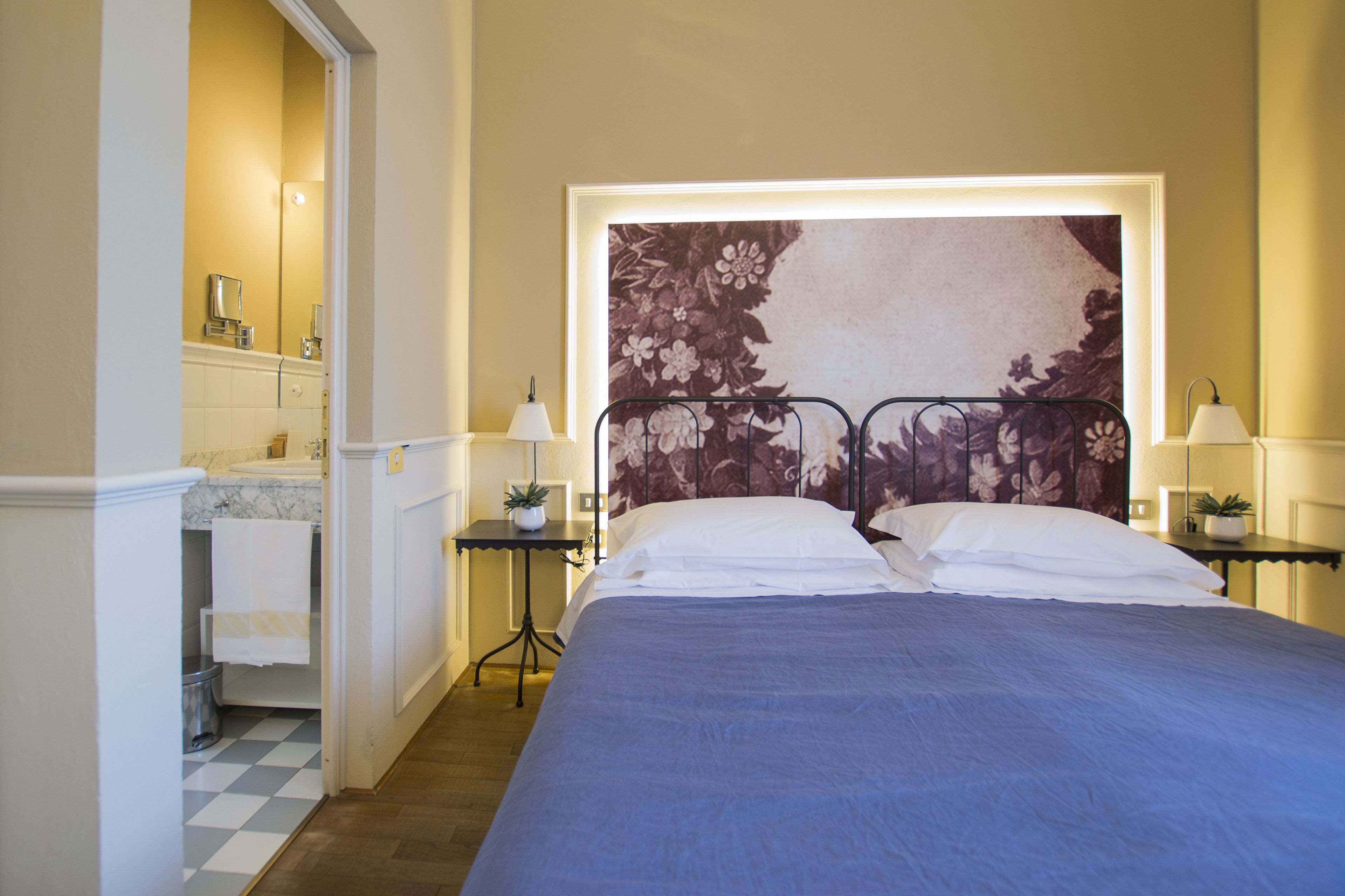 A bedroom with a large bed, a nightstand, a mirror, and a bathroom visible through an open door.
