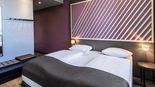 Una habitación de hotel moderna con una cama grande, un escritorio y un televisor montado en la pared.