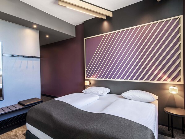A modern hotel room with a large bed, a desk, and a wall-mounted TV.