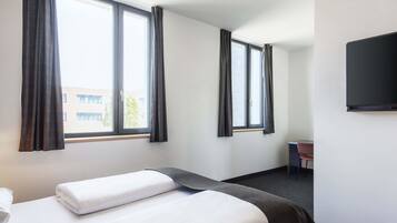 A hotel room with two beds, large windows with curtains, a flat-screen TV, and a desk.